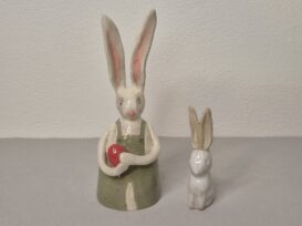 Hase ca.12cm groß hat ein rotes Ei in den Pfoten, die Ohren stehen in die Höhe und sind innen rosa gefärbt. Er trägt eine grüne Hose. Der 2.te Hase ist klein, sehr schlicht und weiß glasiert. Beide Hasen dienen als Osterdekoration