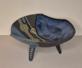 Schale aus Keramik mit drei Beinen, blau-schwarz marmorierter Glasur und einem Zierstreifen mit geometrischen Mustern in hellbraunen, schwarzen und blauen Farbtönen. Die Schale hat ein asymmetrisches, modernes Design.