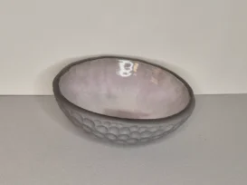 Eine handgefertigte Keramikschale mit einer strukturierten, genoppten grauen Außenseite und einer glatten, hellen lavendelfarbenen Innenseite, die sich vor einem schlichten, hellen Hintergrund abhebt.