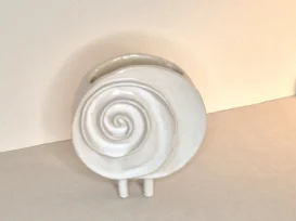 Eine runde, weiße Keramikvase mit einem Spiralmuster auf der Vorderseite, die auf zwei kurzen Beinen aufrecht vor einem neutralen Hintergrund steht.